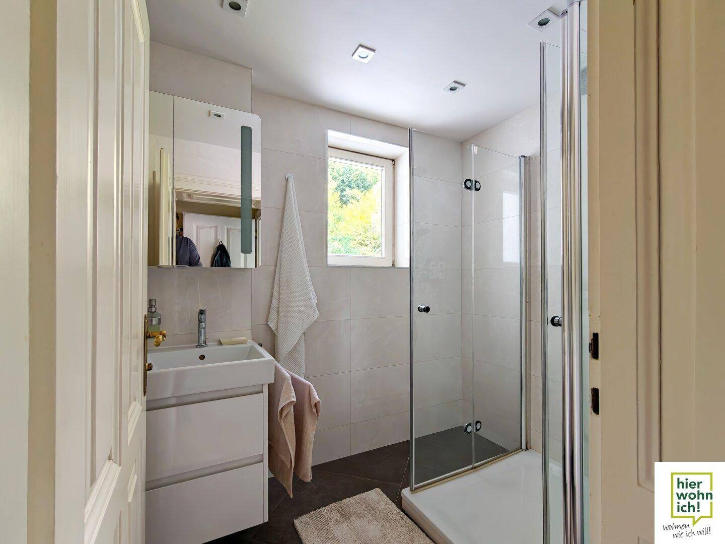 Modernes Badezimmer mit Dusche, Waschbecken und Fenster für Tageslicht.