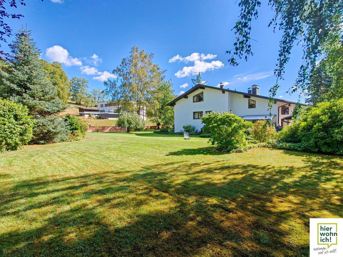 Weitläufiger grüner Garten mit Rasenfläche und einem großen Einfamilienhaus im Hintergrund.