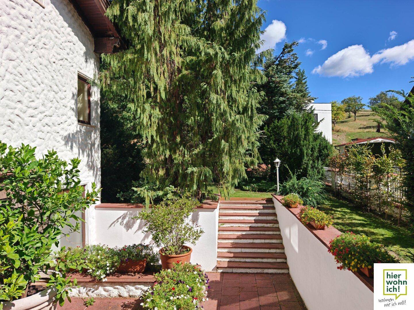 Außenbereich mit Steintreppe, bepflanzten Mauern und Zugang zum weitläufigen Garten.