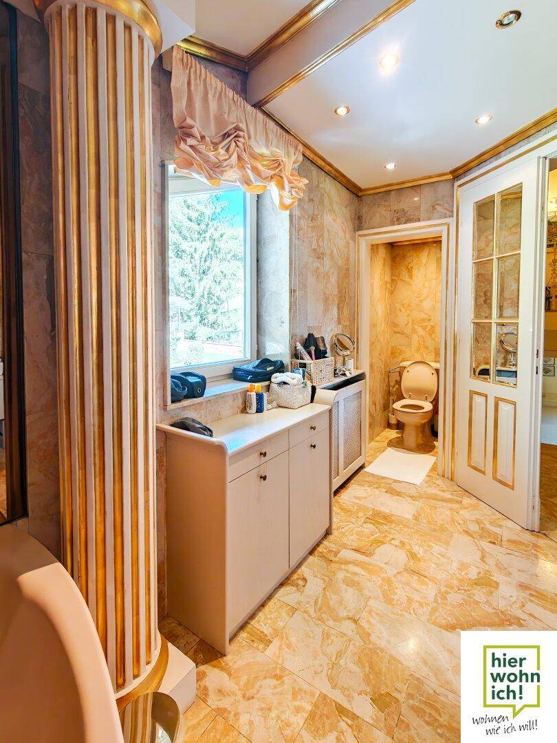Luxuriöses Badezimmer mit Marmorfliesen, goldenen Säulen und separatem WC-Bereich.