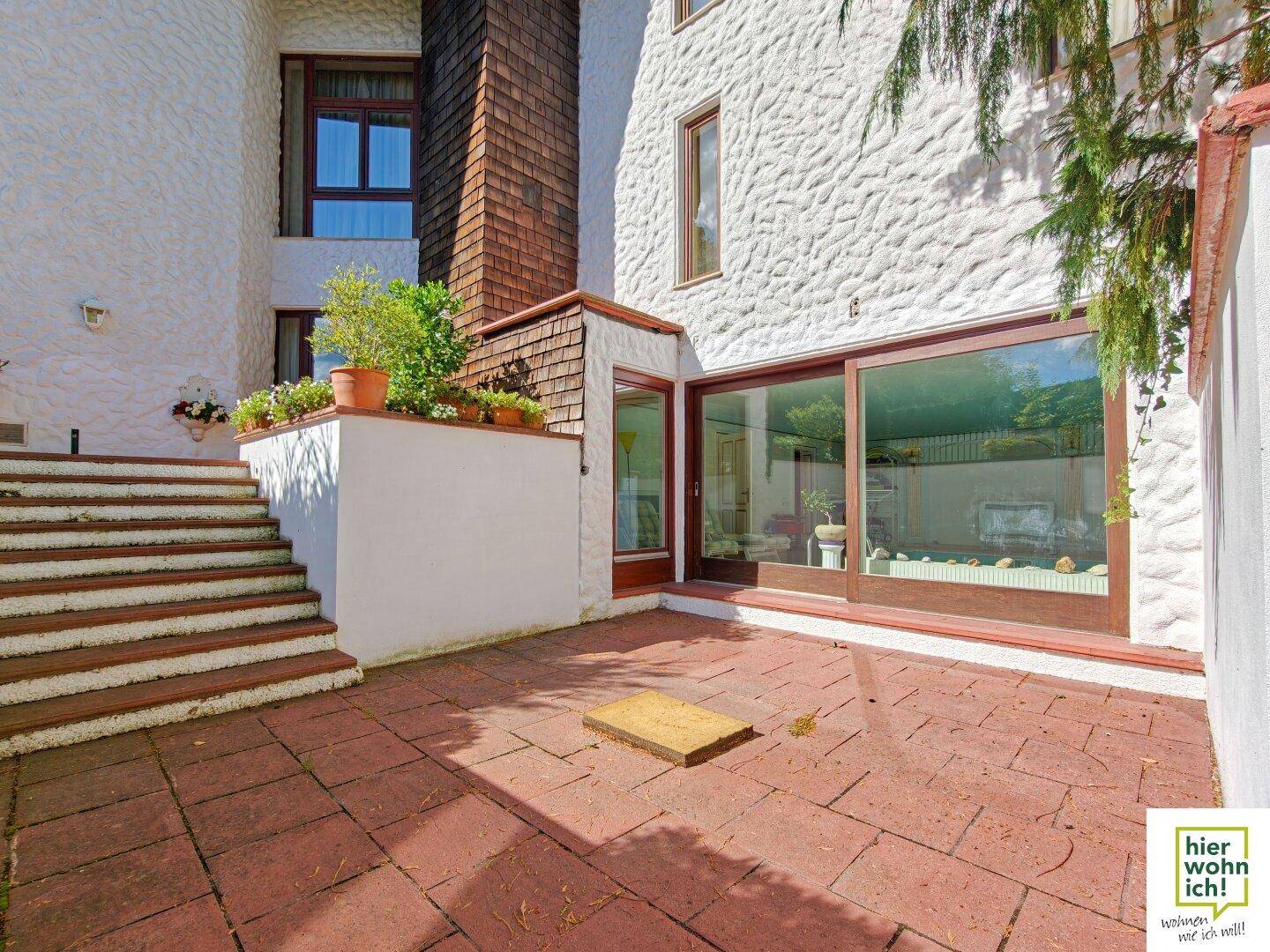 Gepflasterte Terrasse mit Stufen, die zum Haus führen, und großen Fenstern.