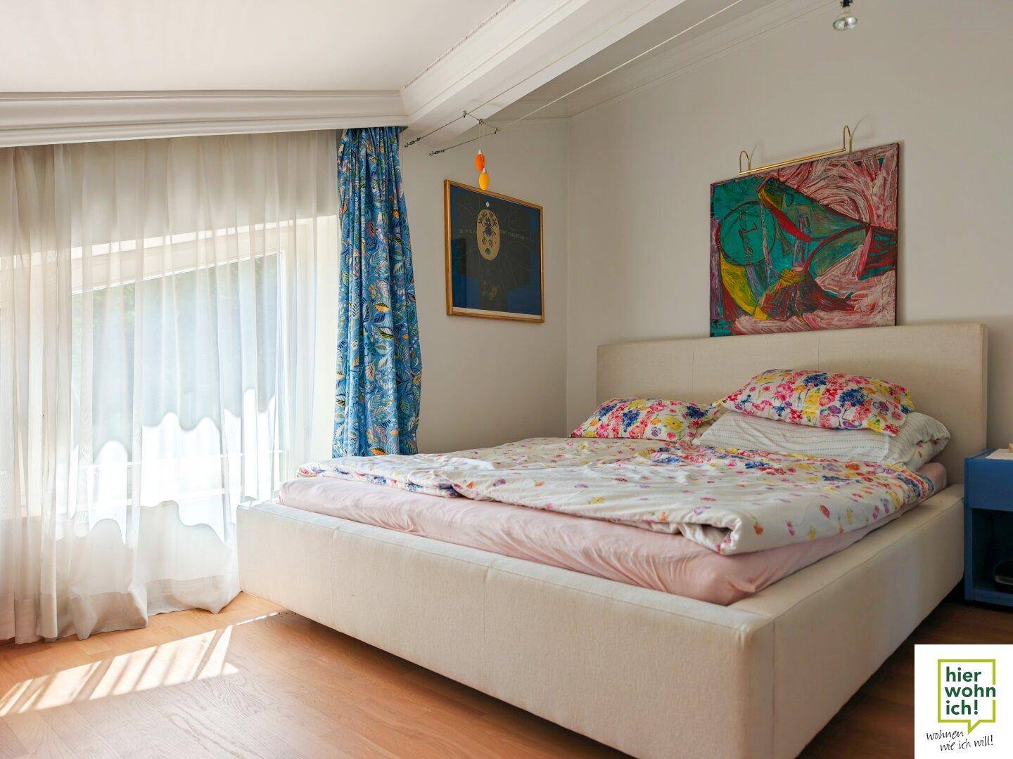 Helles Schlafzimmer mit Holzboden, einem großen Bett und farbenfrohen Kunstwerken an den Wänden.
