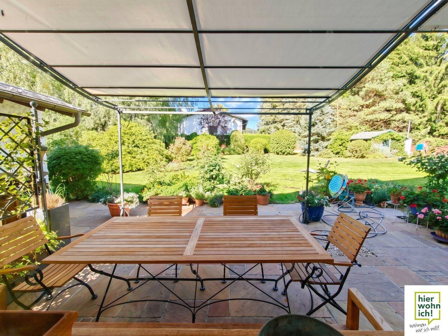 Große überdachte Terrasse mit Holztisch und Stühlen, ideal für Mahlzeiten im Freien.