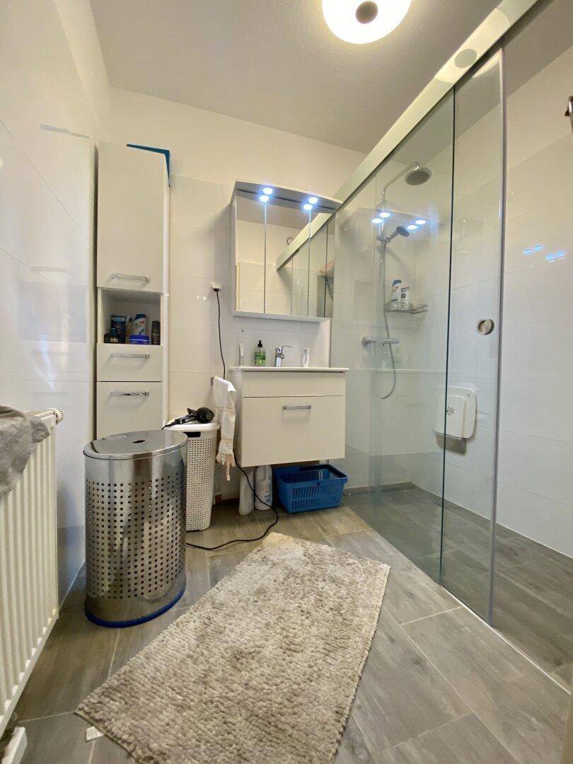 Modernes Badezimmer mit begehbarer Dusche, weißen Fliesen und Waschtischunterschrank.