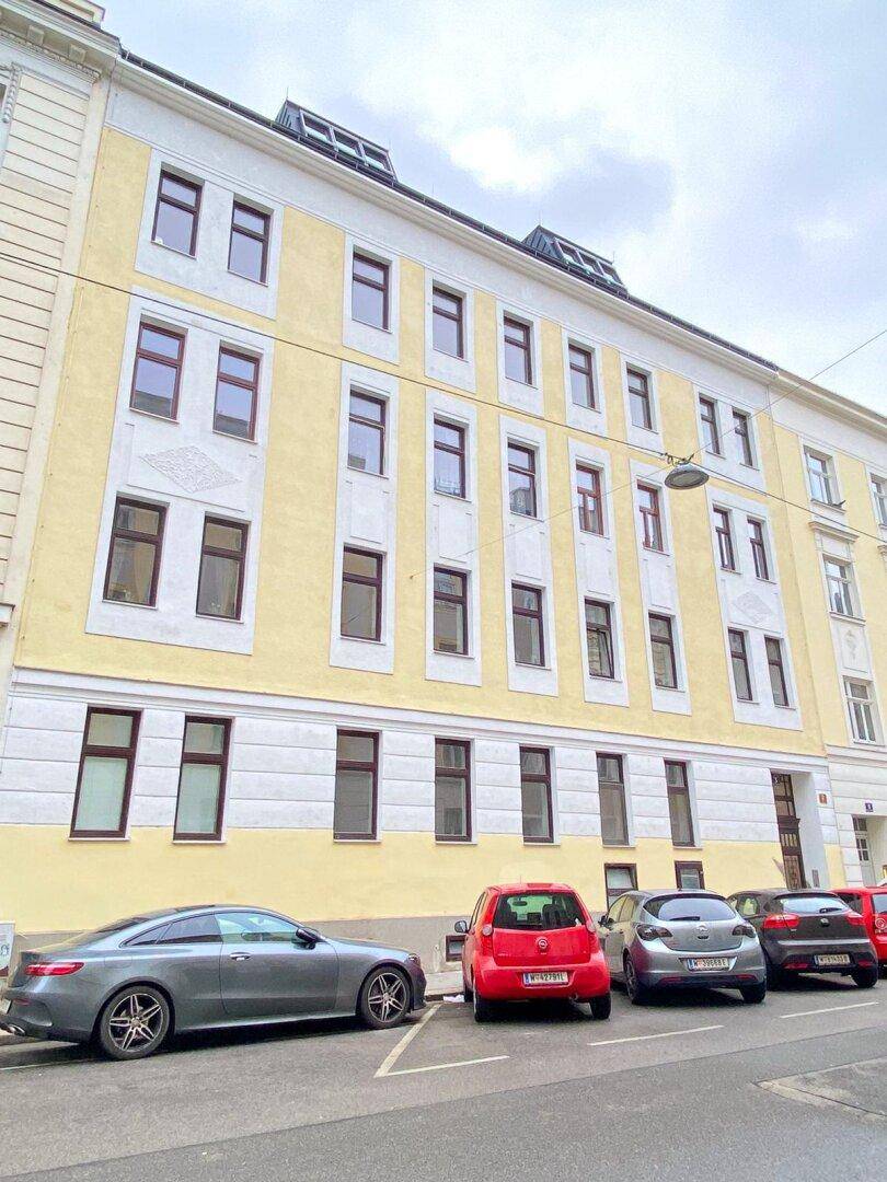 Gut erhaltenes Mehrfamilienhaus mit gelber Fassade, Mansarddach und Dachfenstern in städtischer Umgebung.