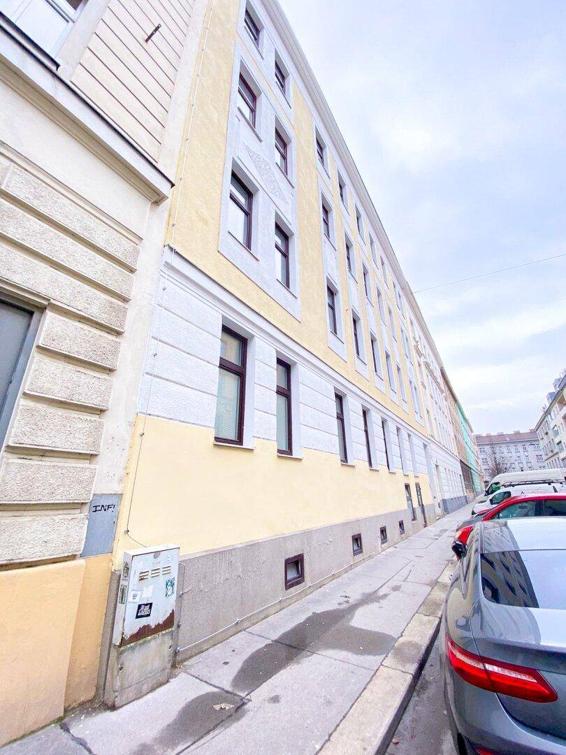 Historisches Mehrfamilienhaus mit gelber Fassade und vielen Fenstern an einer Straße.