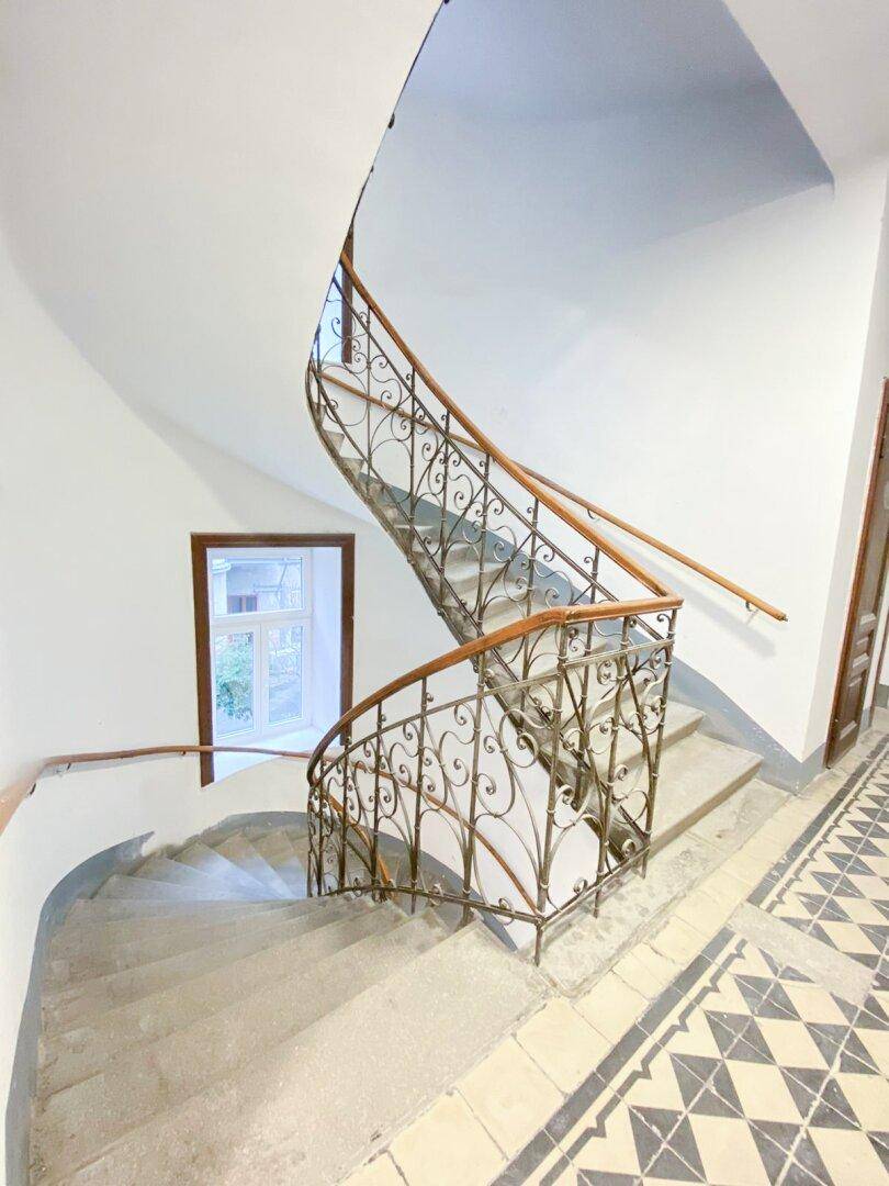 Detailansicht der kunstvollen Wendeltreppe mit schmiedeeisernem Geländer und Holzhandlauf, typisch für historische Gebäude.