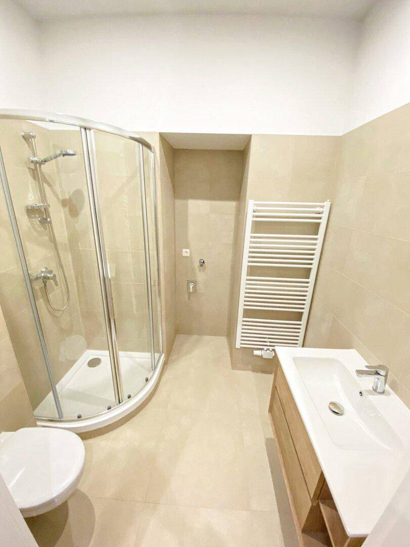 Modernes Badezimmer mit Duschkabine, WC, Waschtisch und beheiztem Handtuchhalter in hellen Beigetönen.