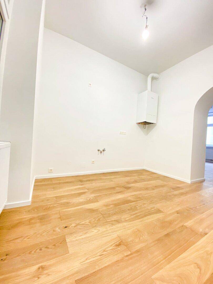 Geräumiger Raum mit Holzfußboden, einem Bogen und einem Wandheizkessel, bietet vielseitige Nutzungsmöglichkeiten.
