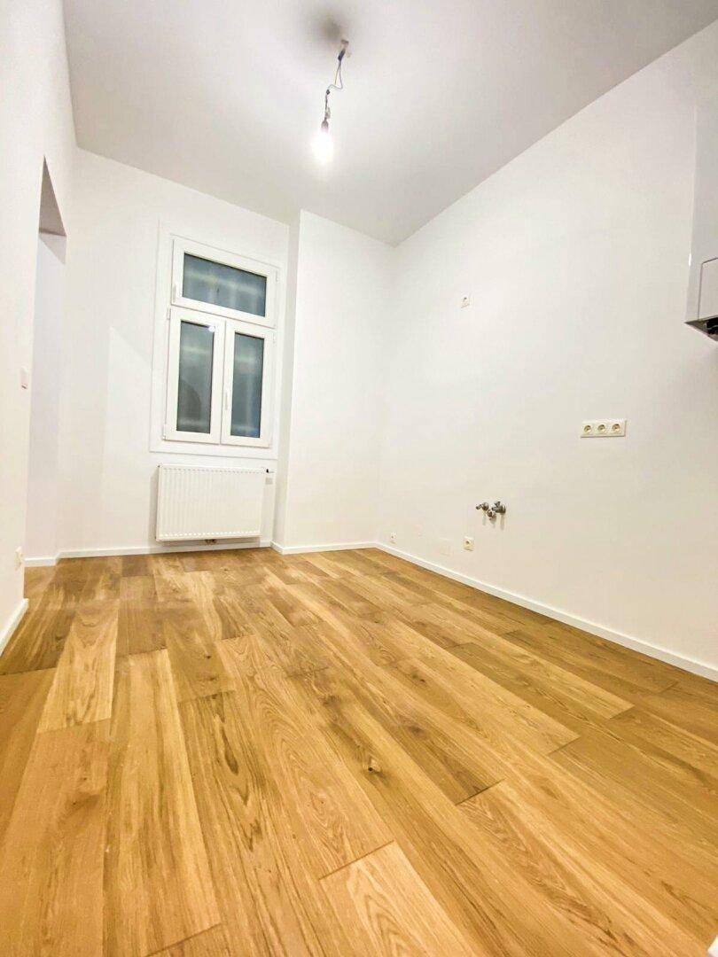 Heller Raum mit Holzfußboden und Fenster, vorbereitet für die Installation einer modernen Küche.