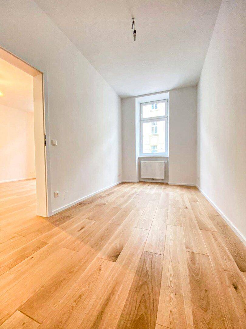Gemütliches Zimmer mit hellem Holzfußboden und einem Fenster, ideal als Schlaf- oder Arbeitszimmer.