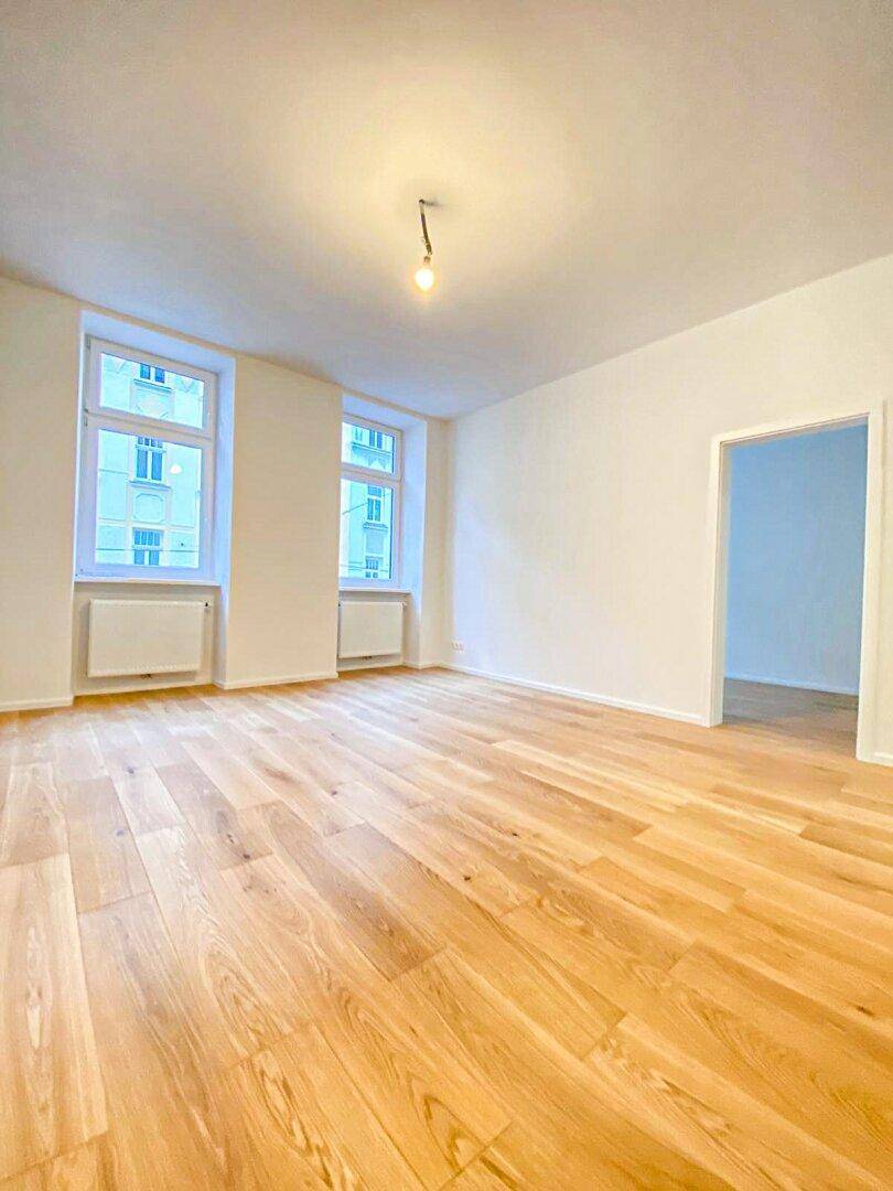 Geräumiges Wohnzimmer mit neuem Holzfußboden und zwei großen Fenstern, sehr hell und einladend.