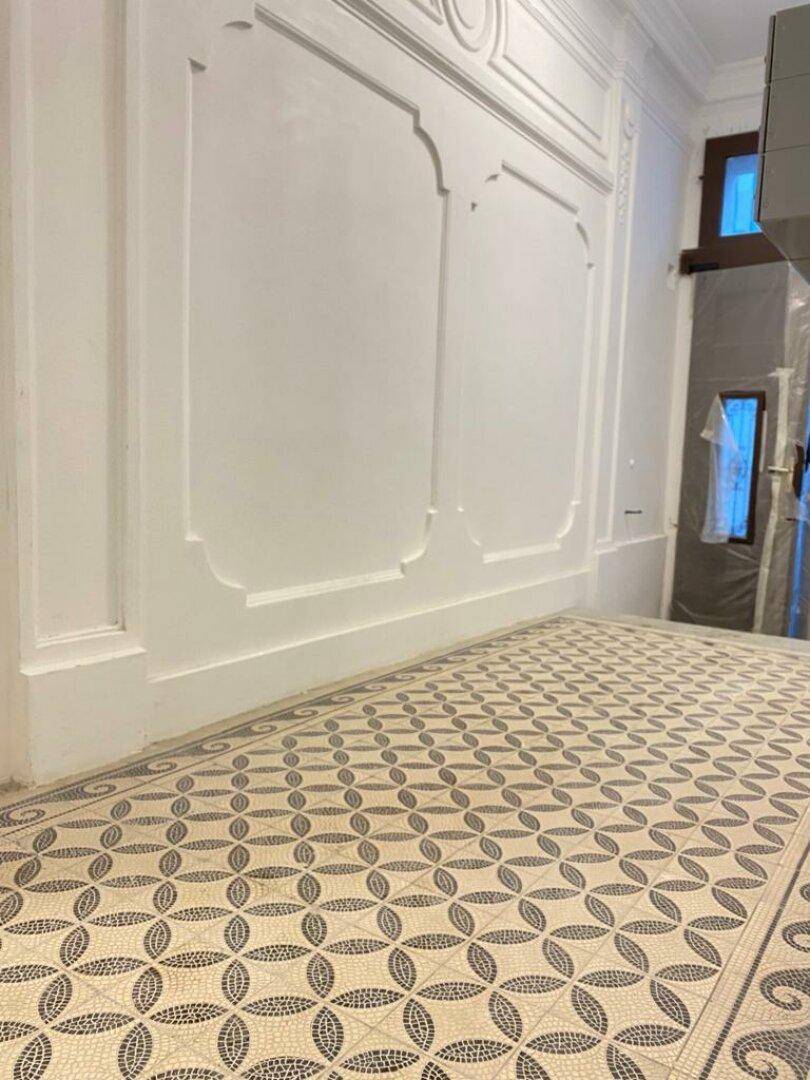 Detailansicht des Flurs mit kunstvollen Wandverzierungen und einem gemusterten Fliesenboden.