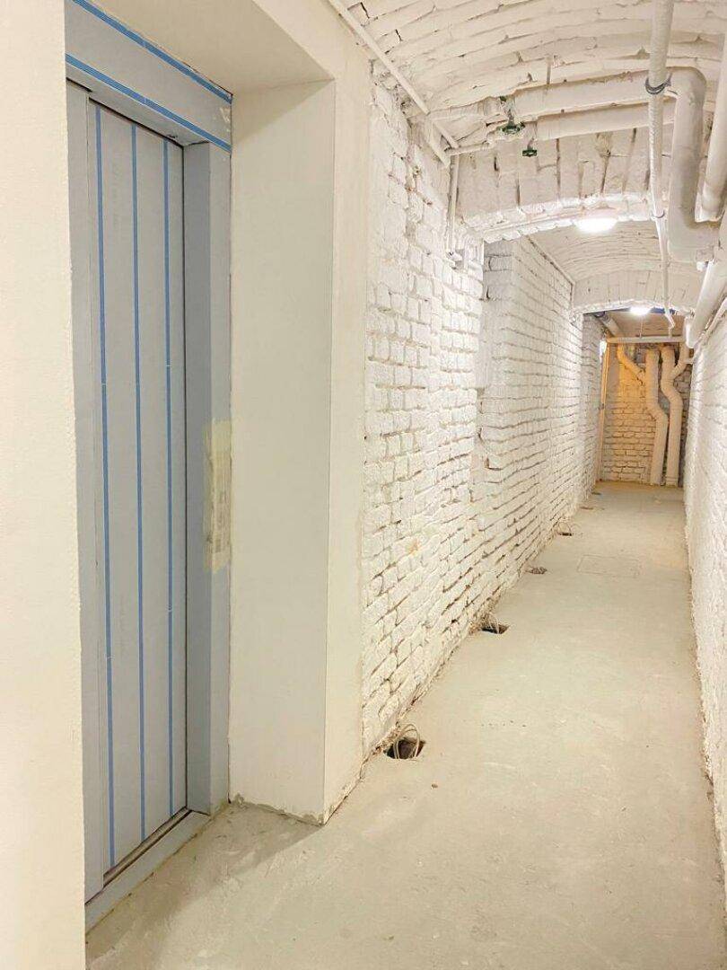 Heller Kellerraum mit weiß gestrichenen Ziegelwänden, Betonboden und sichtbaren Leitungen.
