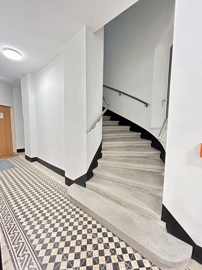 Treppenhaus mit elegantem Geländer und gemustertem Fliesenboden im Eingangsbereich.