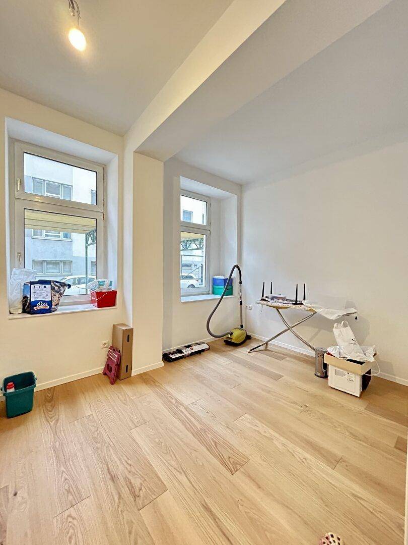 Heller Raum mit Parkettboden und zwei Fenstern, derzeit als Abstell- oder Arbeitsbereich genutzt.