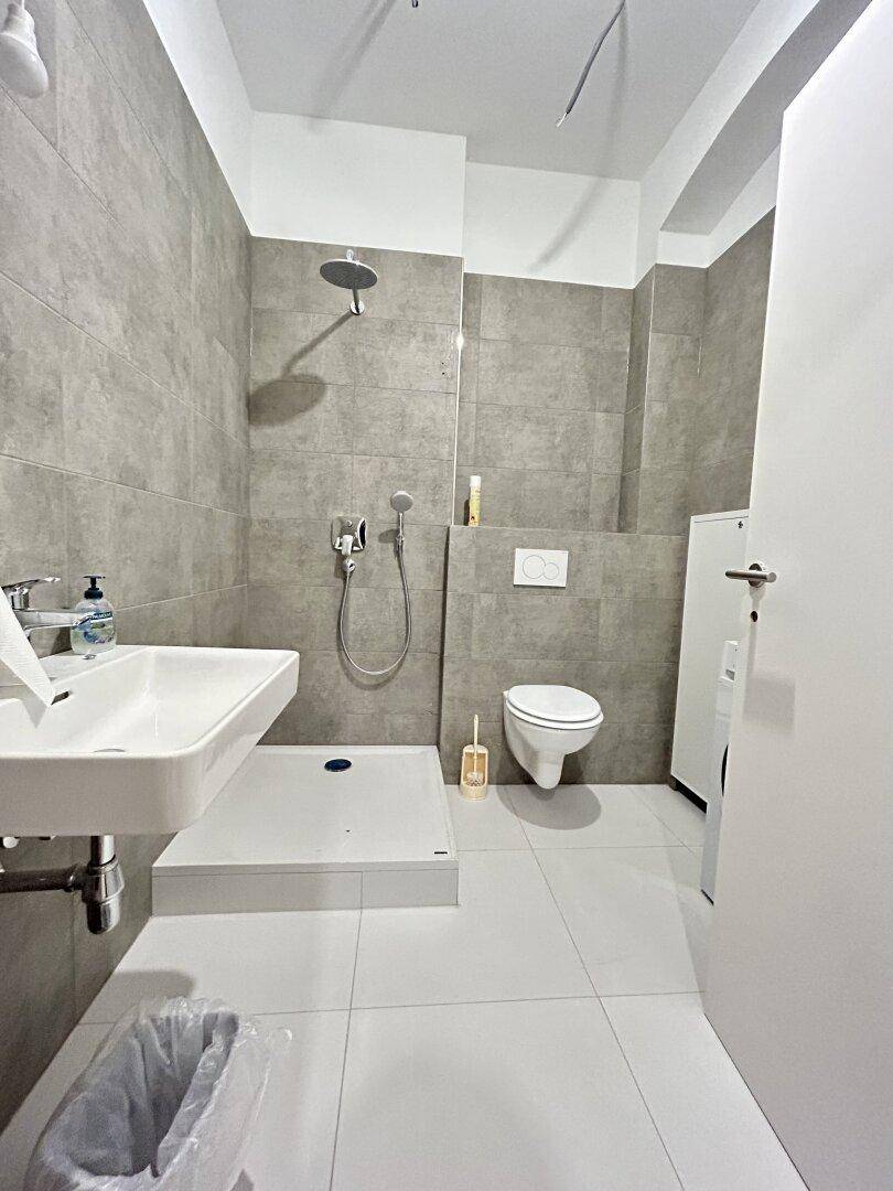 Modernes Badezimmer mit grauen Fliesen, ebenerdiger Dusche und wandhängendem WC.