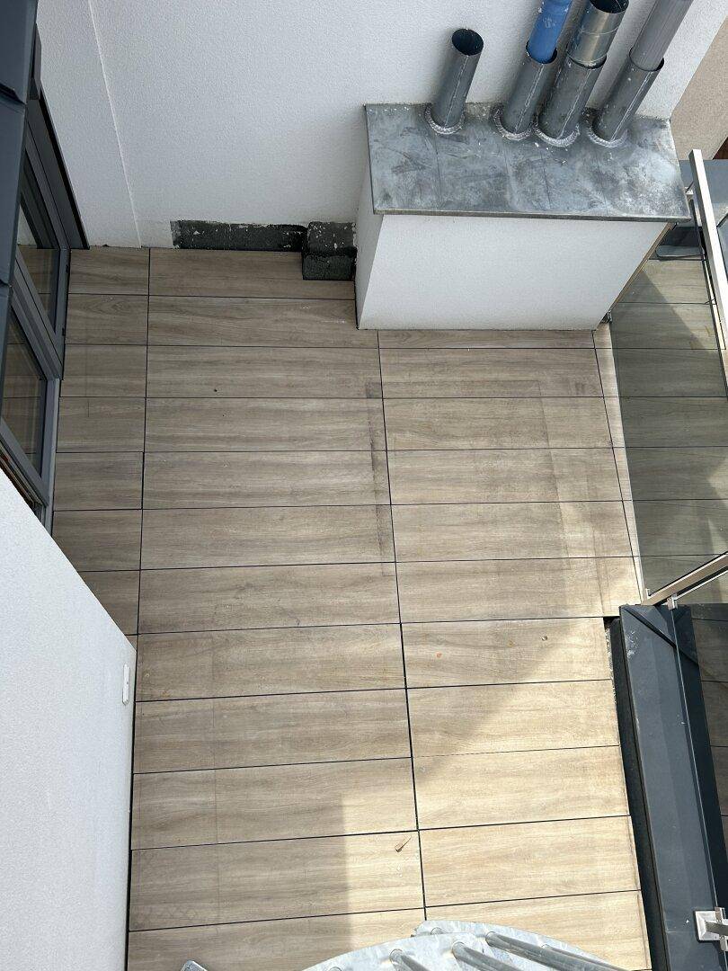 Kleiner Balkon mit Holzfliesen und sichtbaren Rohren, bietet Platz im Freien.