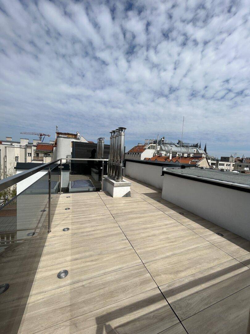 Geräumige Dachterrasse mit Holzfliesen und Blick auf die umliegenden Gebäude.