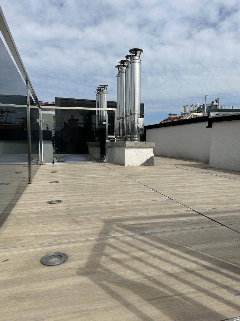 Moderne Dachterrasse mit Bodenstrahlern und Edelstahlkaminen, umgeben von Glasgeländern.