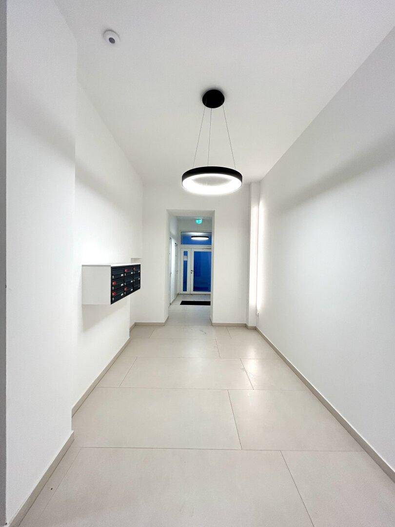 Langer, heller Flur mit modernen Fliesen und Postfächern in einem Neubau.