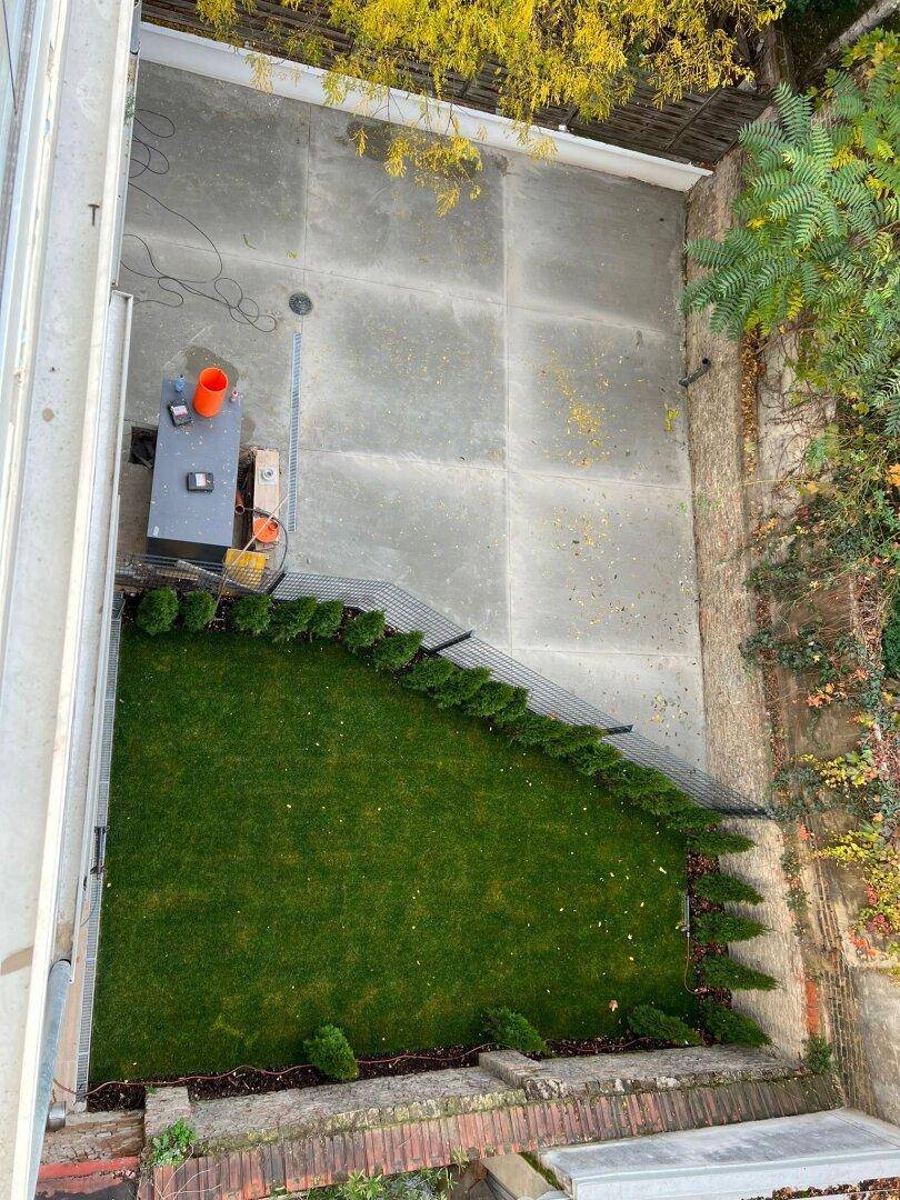 Gepflegter Gartenbereich mit Rasenfläche und gepflastertem Sitzbereich von oben gesehen.
