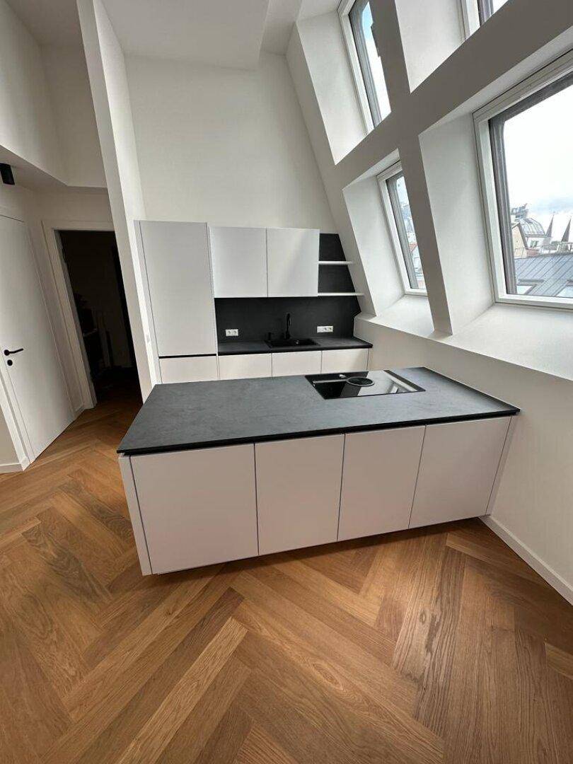 Moderne Küche mit weißen Schränken, dunkler Arbeitsplatte und Fischgrätparkett unter Dachschrägen.