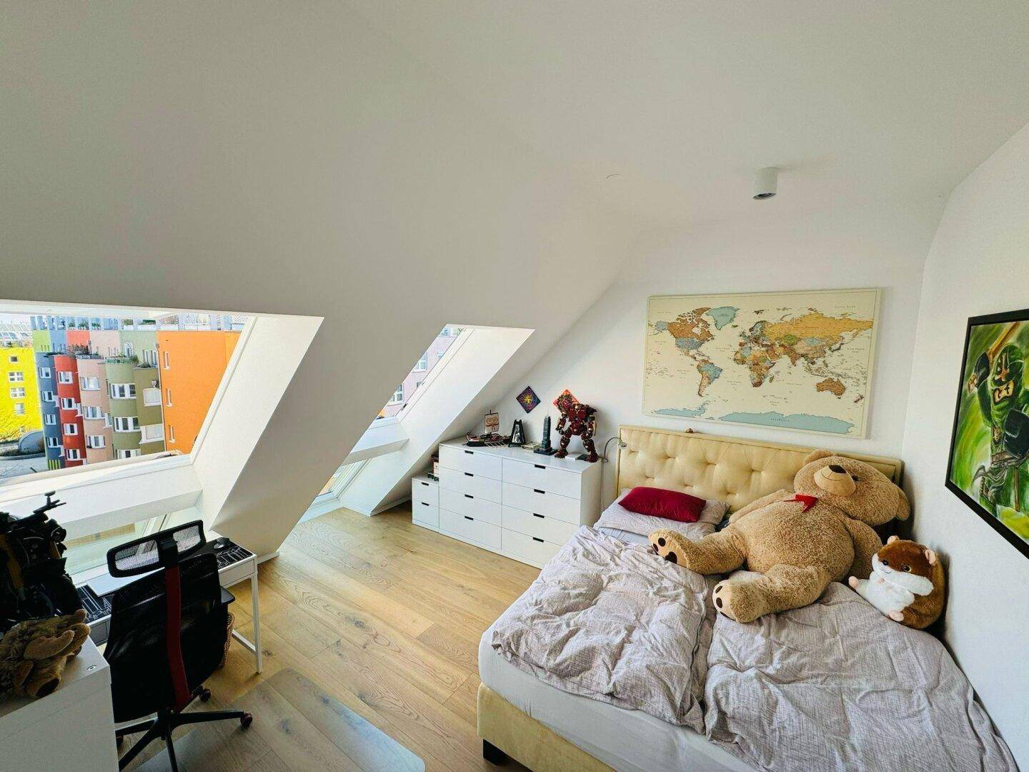 Helles Schlafzimmer unter einer Dachschräge mit Holzboden und großen schrägen Fenstern.
