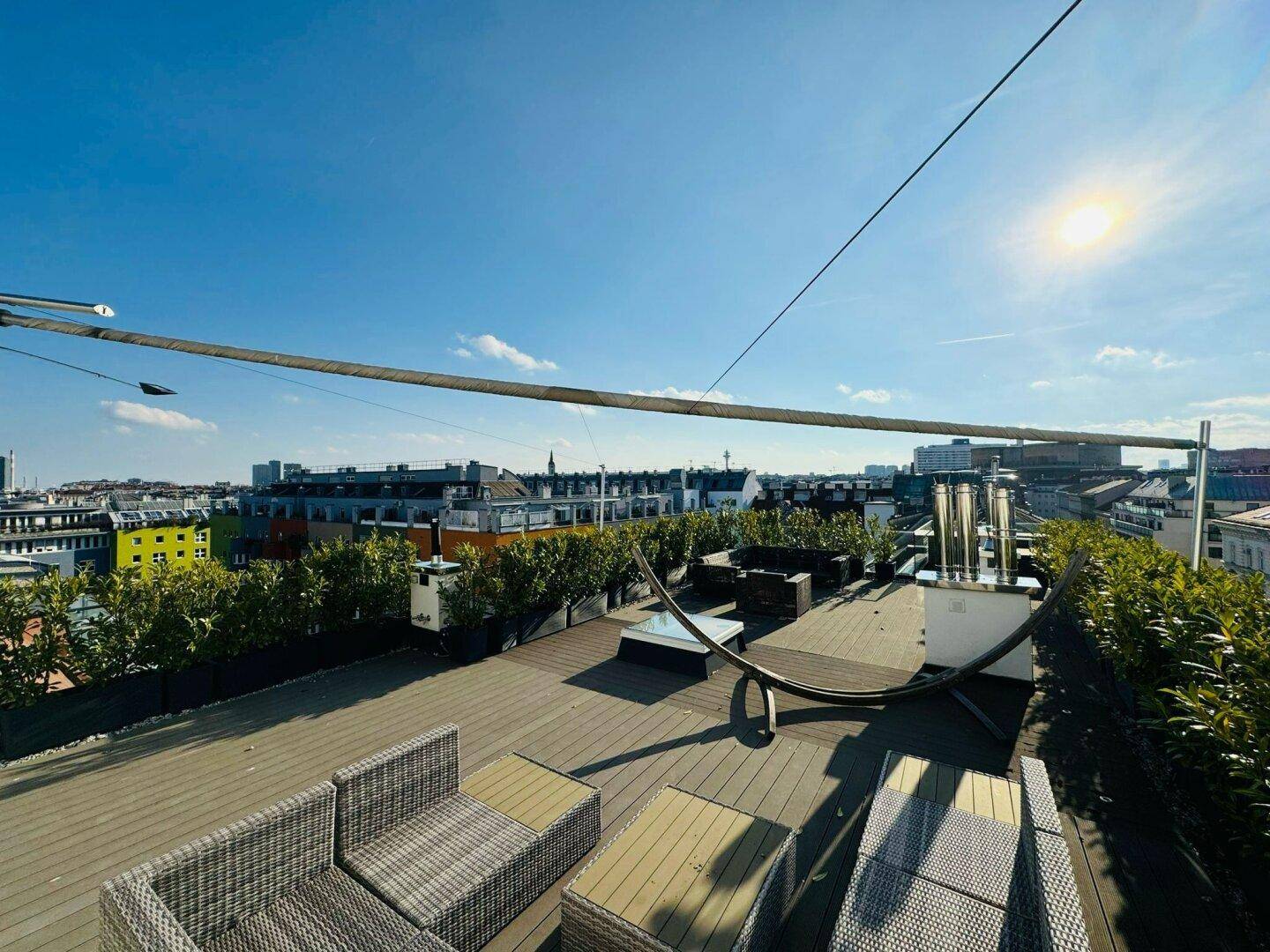 Obere Dachterrasse mit Lounge-Möbeln, Pflanzen und Panoramablick auf die Stadt.