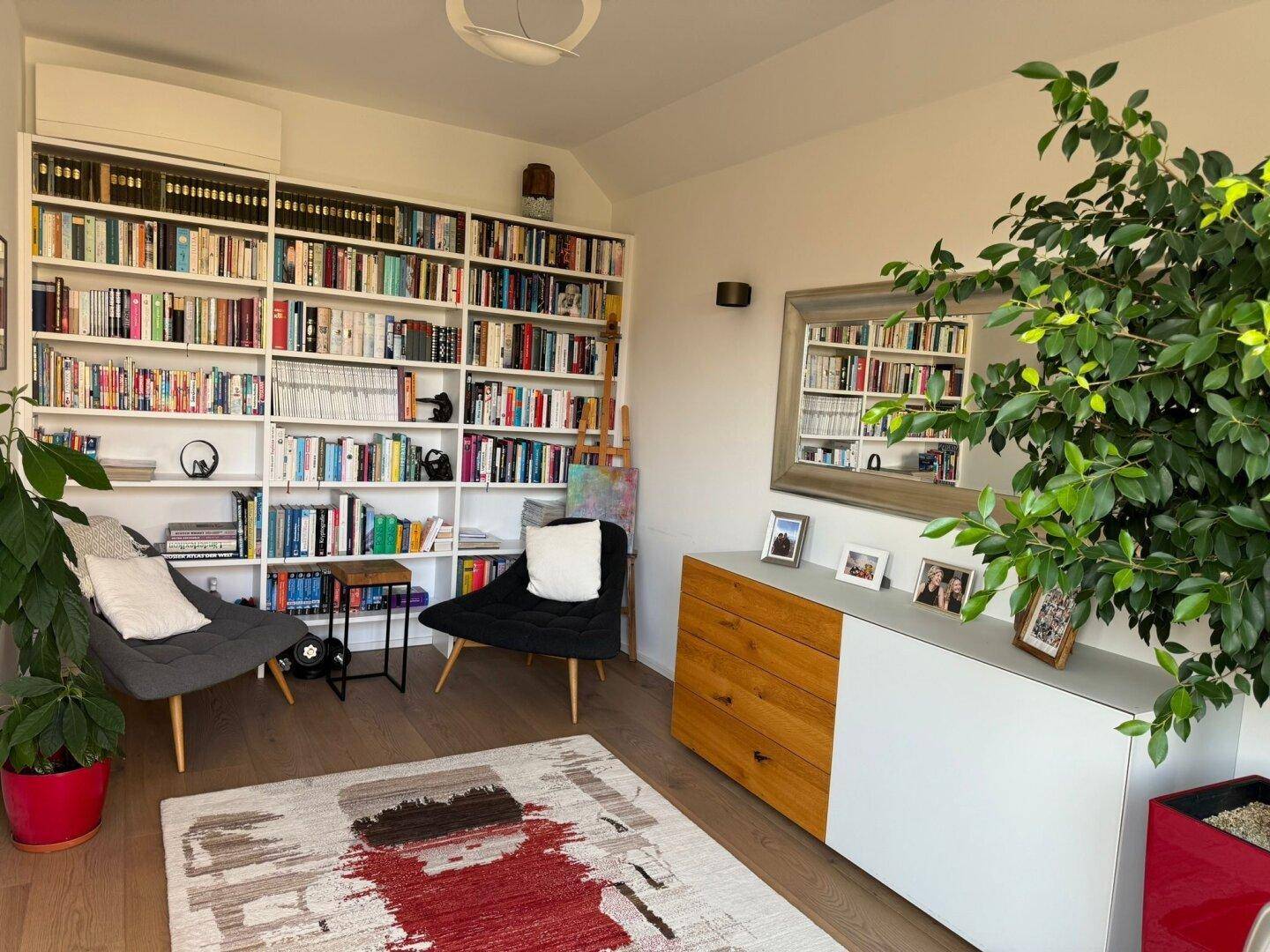 Helles Arbeitszimmer mit großer Bücherwand, Holzboden und bequemen Sesseln.