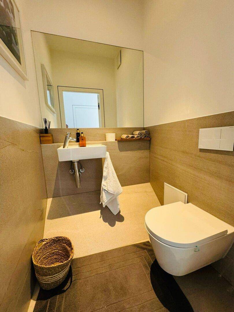 Modernes Gäste-WC mit Wand-WC, kleinem Waschbecken und Fliesenboden.