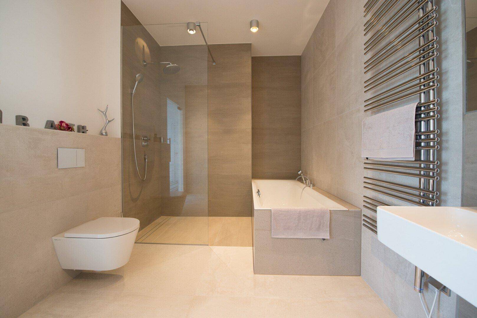 Modernes Badezimmer mit begehbarer Dusche, Badewanne, Wand-WC und beheiztem Handtuchhalter.