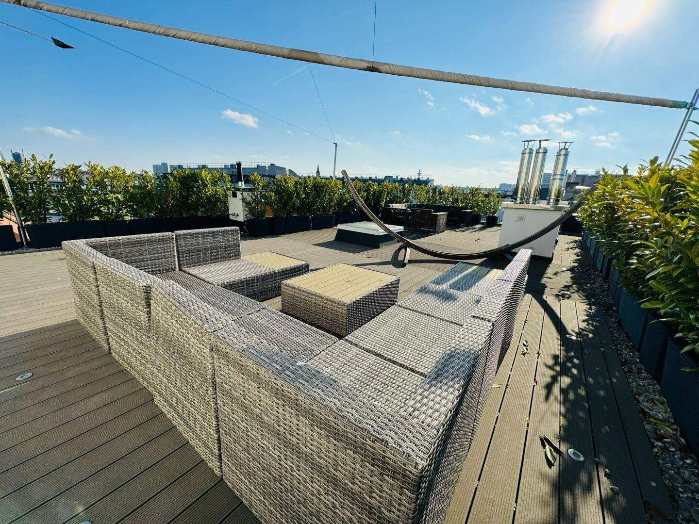 Obere Dachterrasse mit bequemen Lounge-Möbeln und weitem Blick unter blauem Himmel.