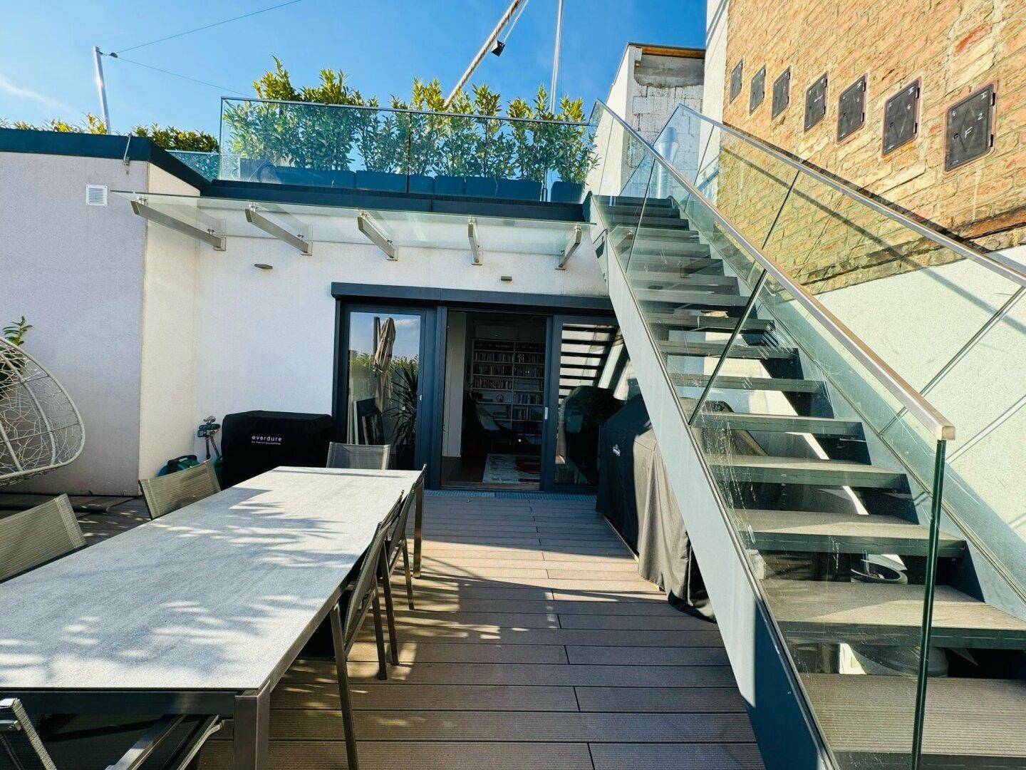 Untere Dachterrasse mit Esstisch und moderner Treppe, die zur oberen Ebene führt.