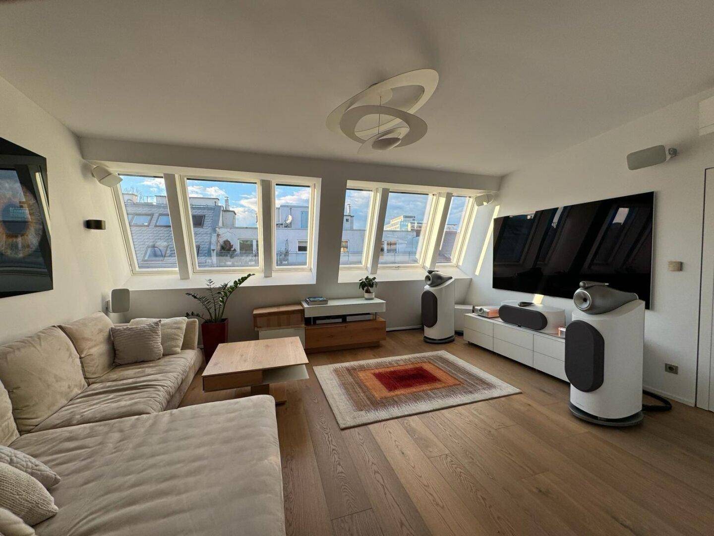 Helles Wohnzimmer mit schrägen Fenstern, Holzboden und moderner Einrichtung unter einer Dachschräge.