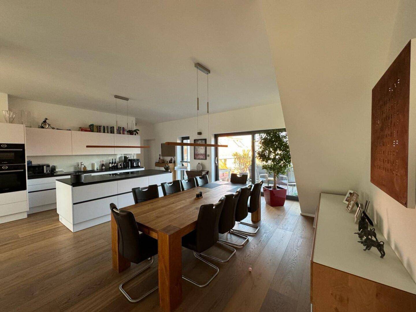 Offener Wohn- und Essbereich mit moderner Einbauküche, großem Esstisch und Zugang zur Terrasse.