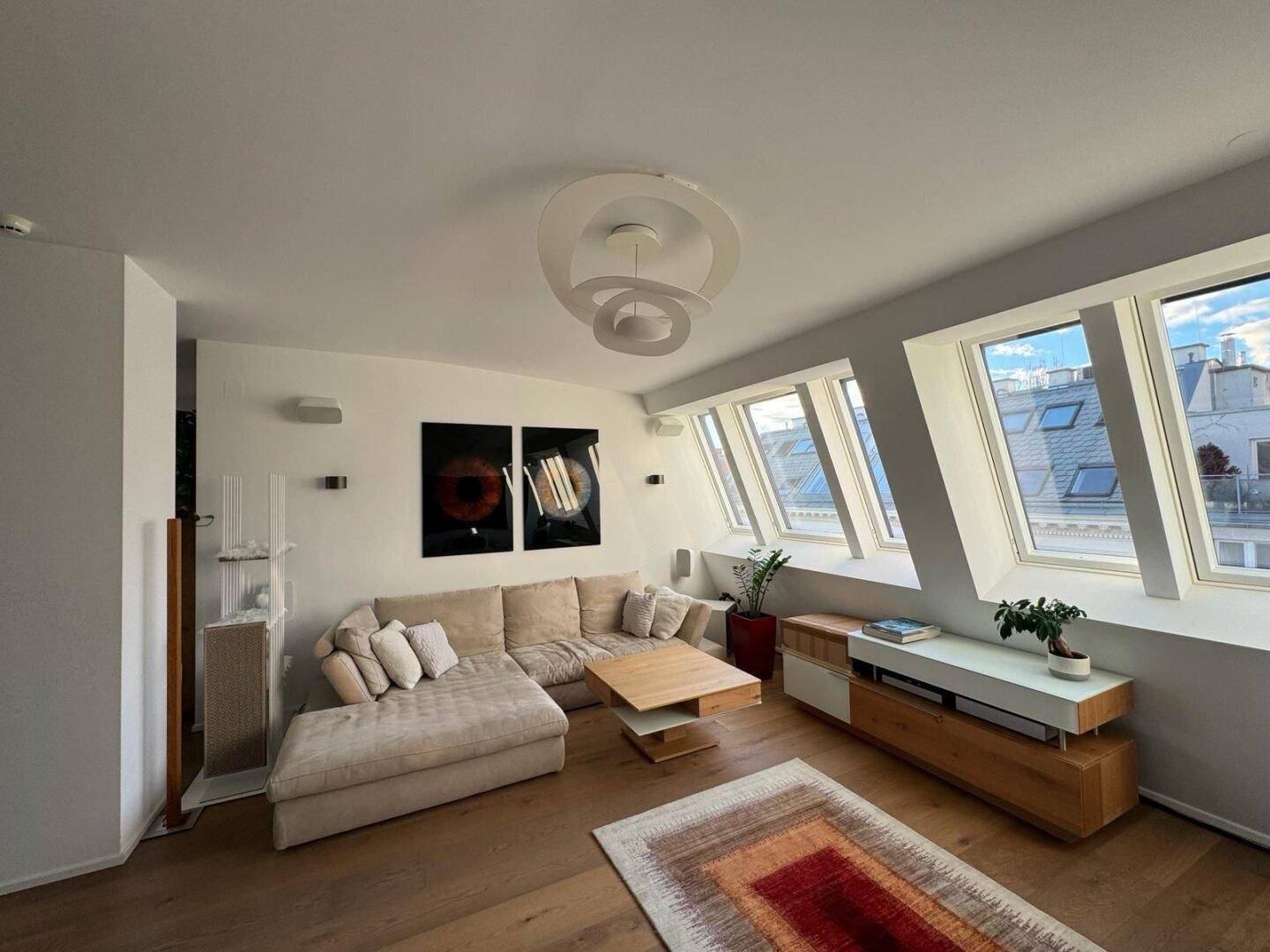 Helles Wohnzimmer mit schrägen Fenstern, gemütlichem Sofa und Holzboden.