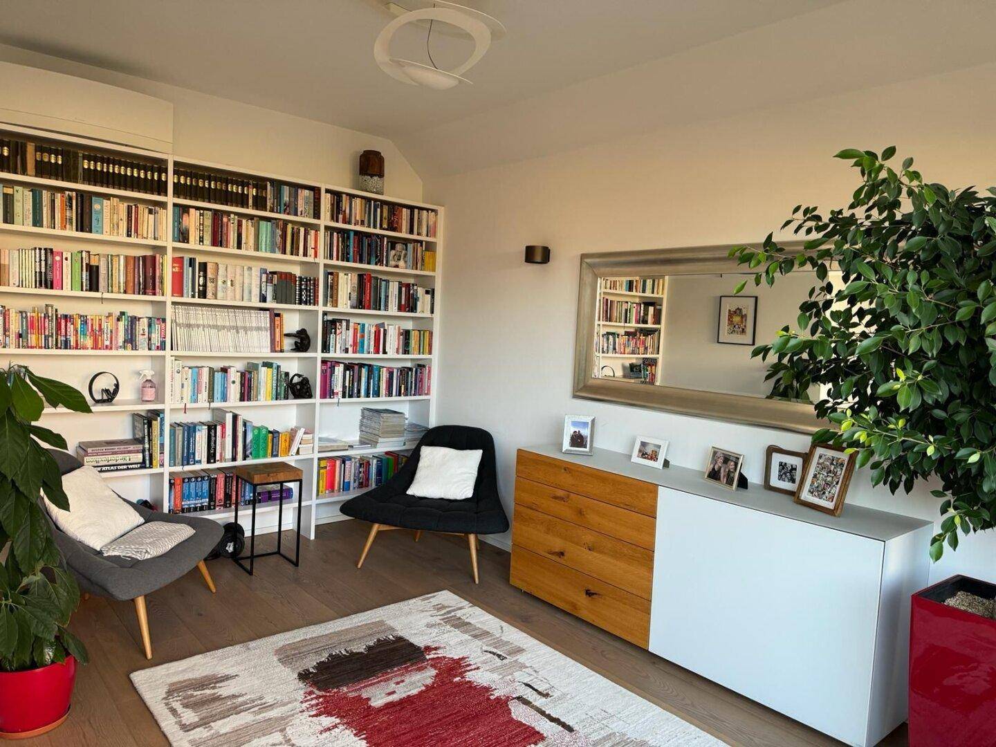 Helles Arbeitszimmer mit umfangreicher Bücherwand, bequemen Sesseln und Holzboden.