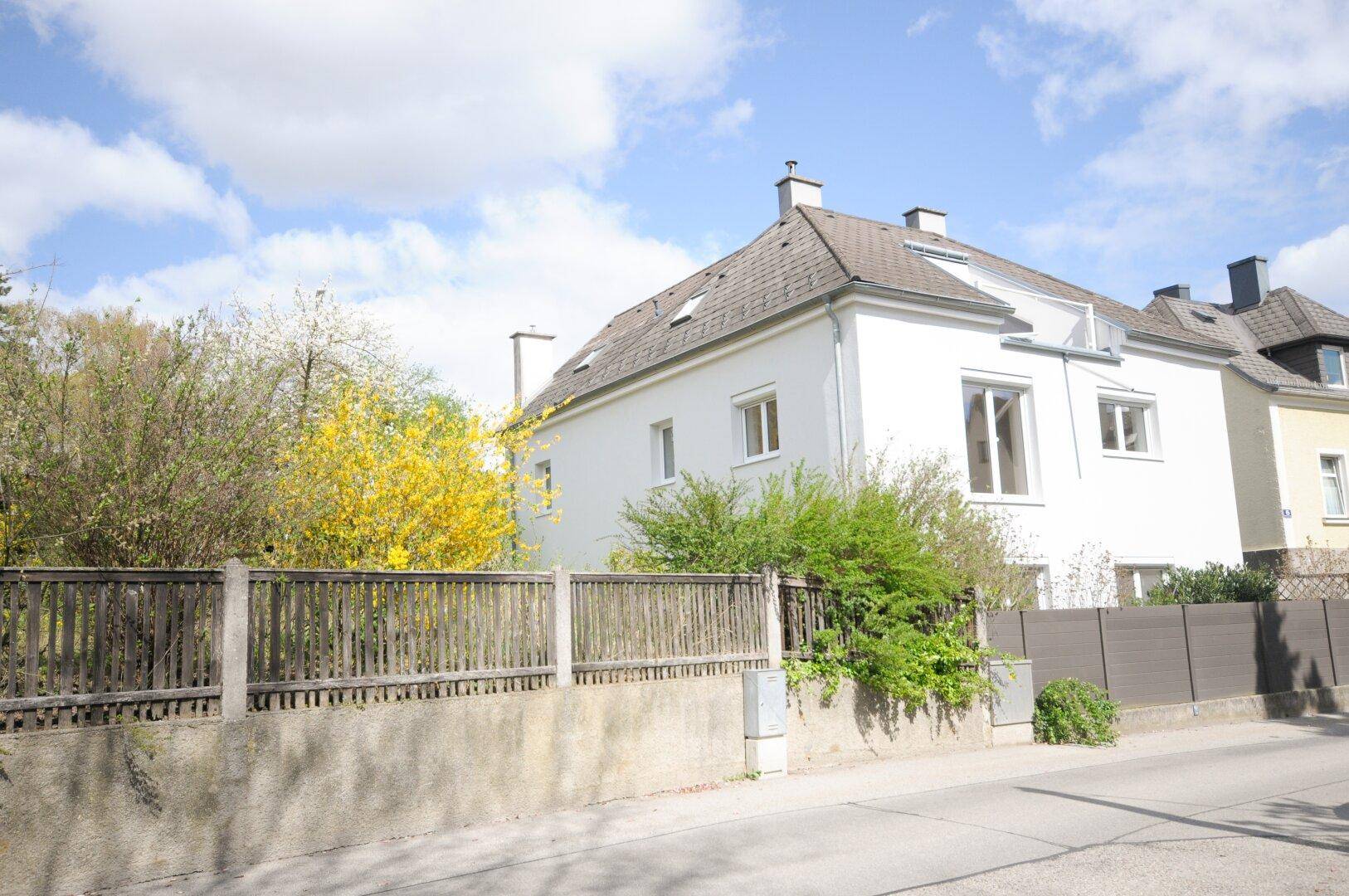 Weißes Wohnhaus mit Satteldach und umzäuntem Vorgarten in einer ruhigen Wohngegend.