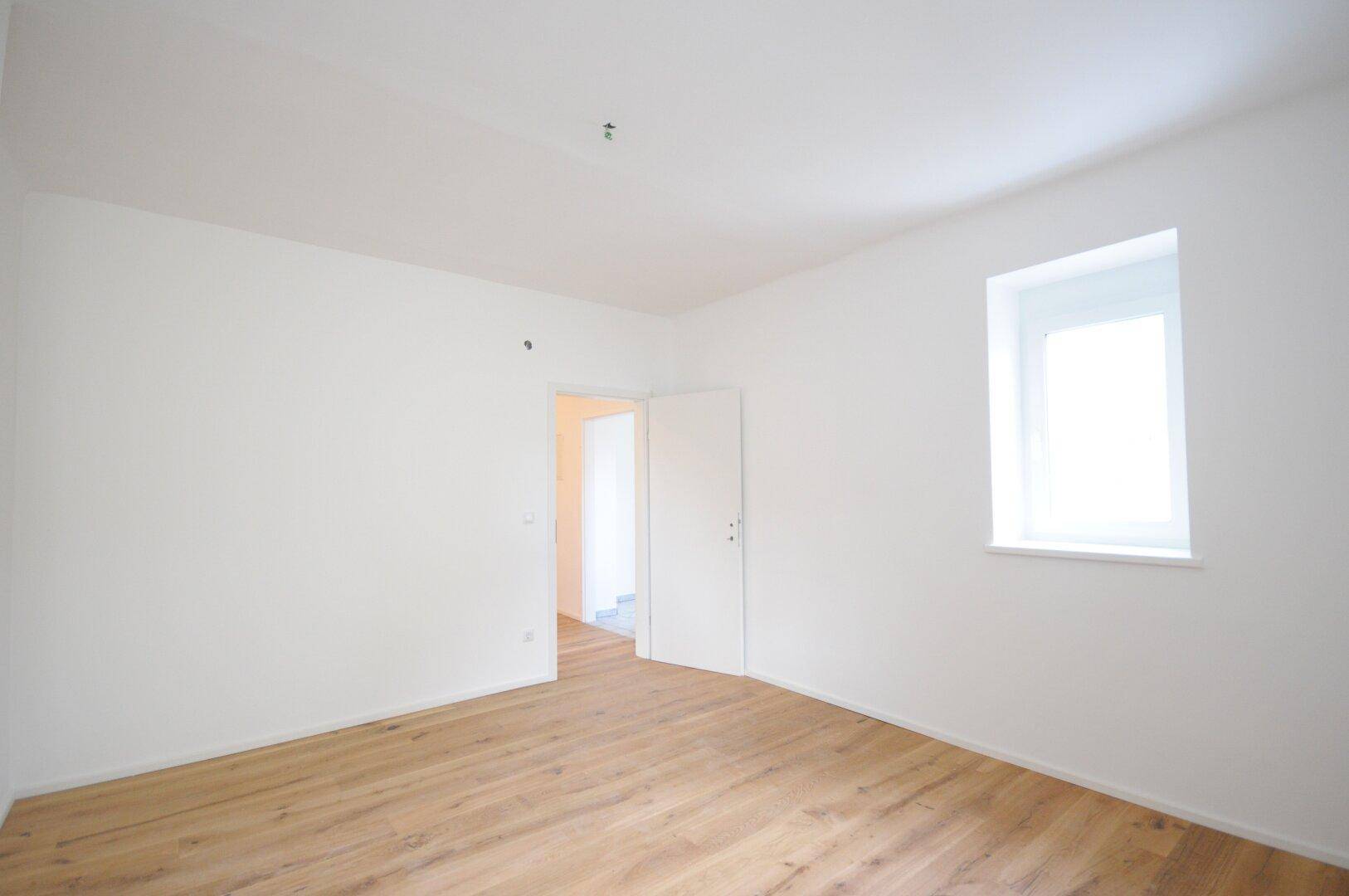 Helles Schlafzimmer mit Holzboden und einem Fenster, das viel Tageslicht hereinlässt.