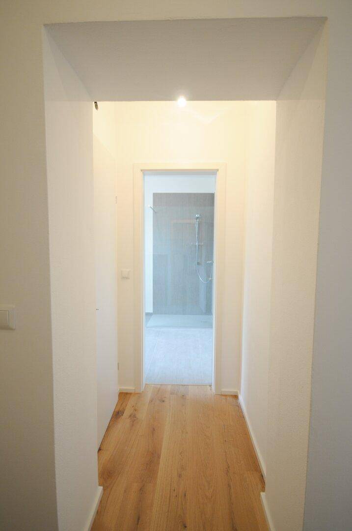 Langer, heller Flur mit Holzboden, der zu einem Badezimmer oder weiteren Räumen führt.