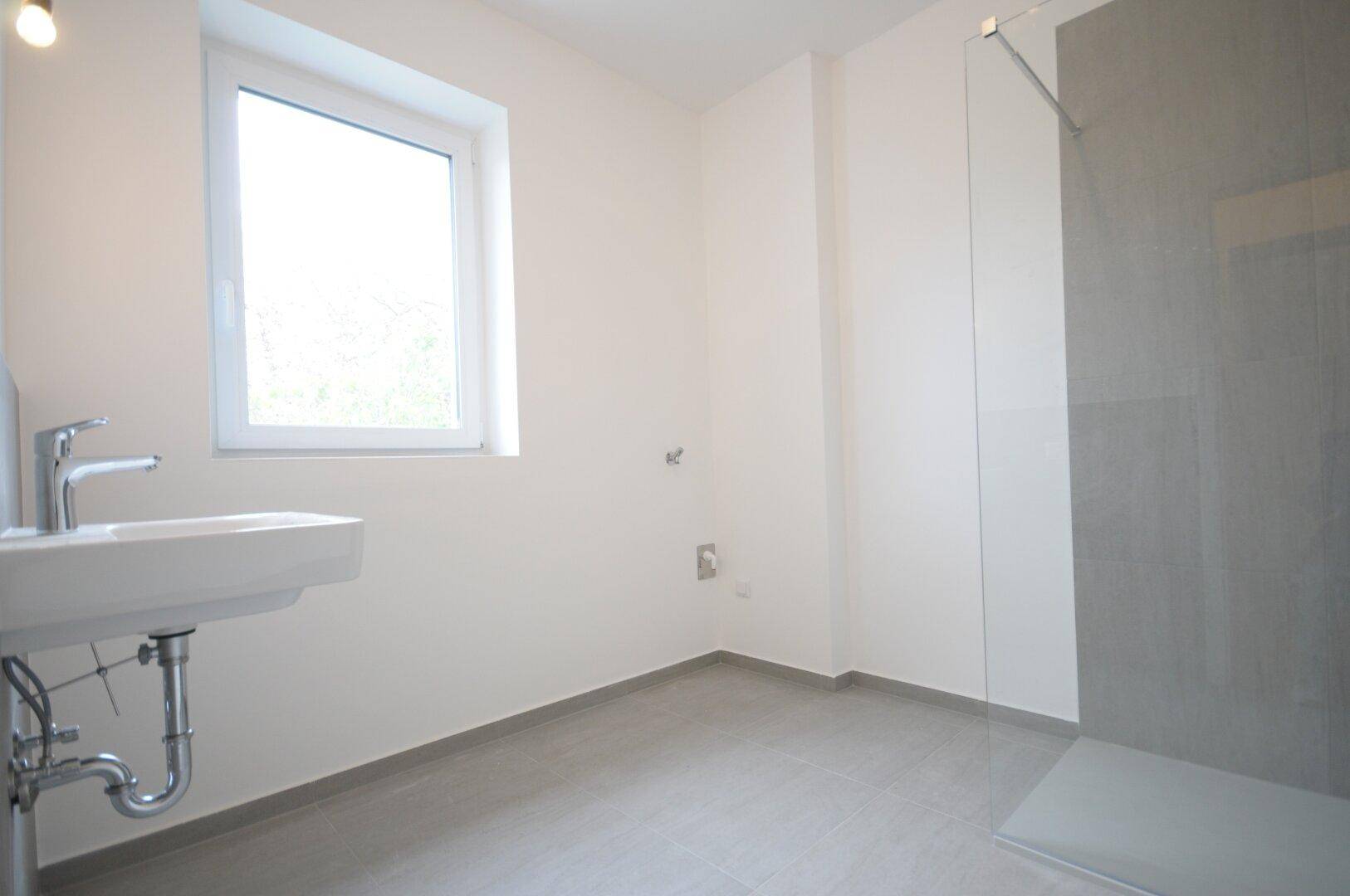 Modernes Badezimmer mit Dusche, Waschbecken und Fenster, das für natürliche Belüftung sorgt.