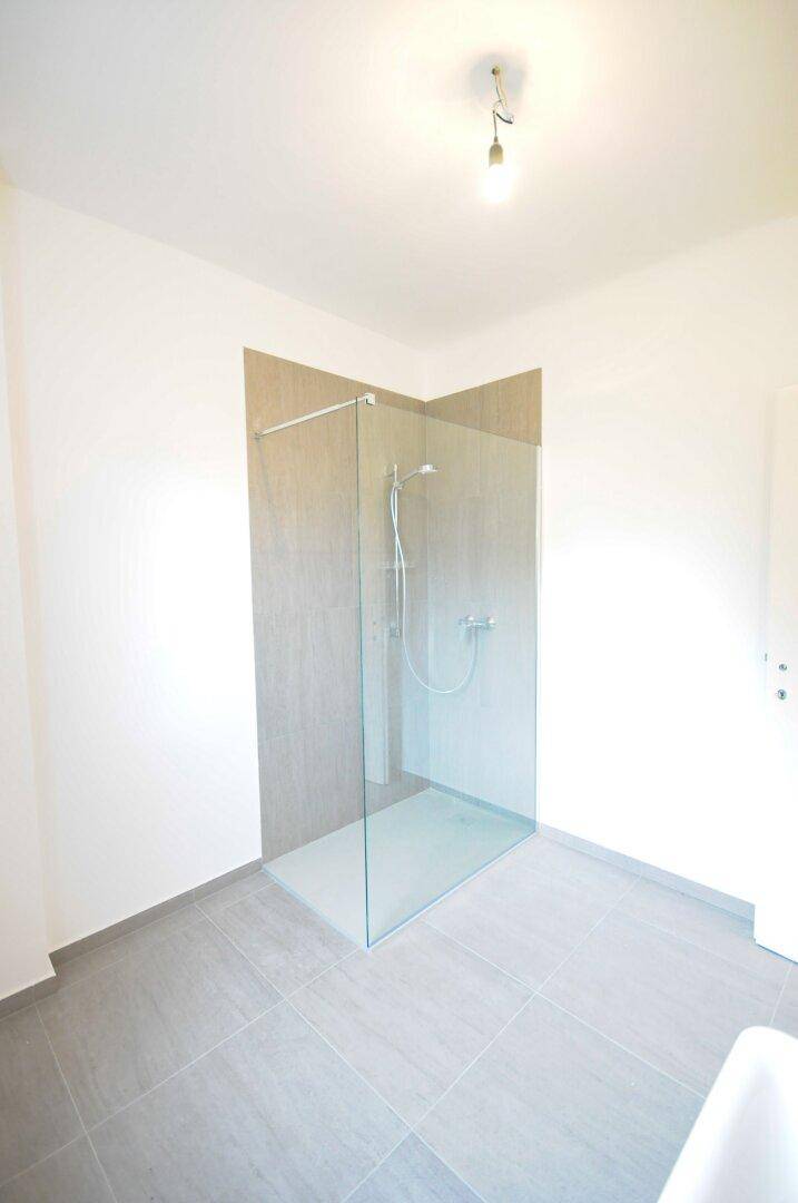 Modernes Badezimmer mit geräumiger Glasdusche und grauen Bodenfliesen.