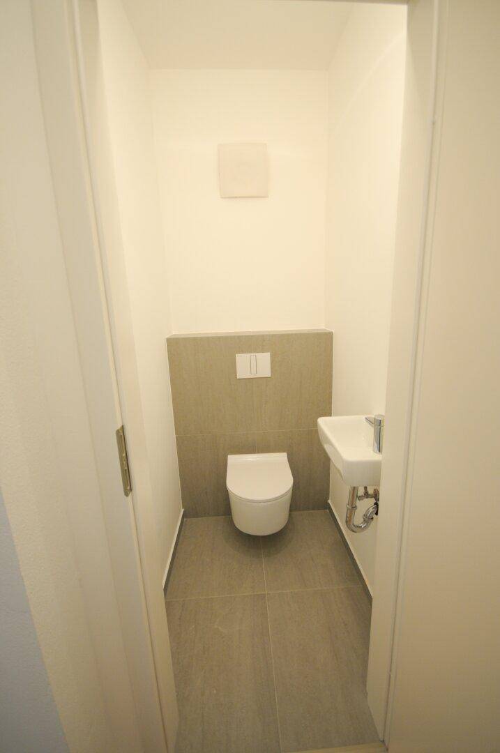 Kleines Gäste-WC mit wandhängender Toilette, Waschbecken und modernen Fliesen.