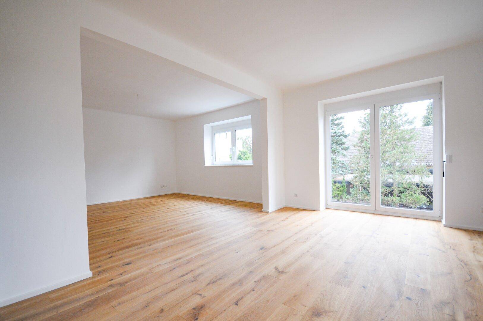 Großzügiger Wohnbereich mit Holzboden und bodentiefen Fenstern, die Zugang nach draußen bieten.