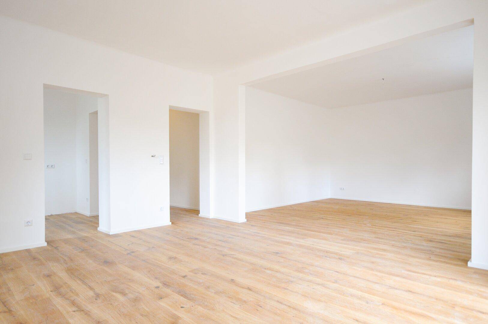 Offener Wohnbereich mit hellem Holzboden und Durchgängen zu angrenzenden Räumen.