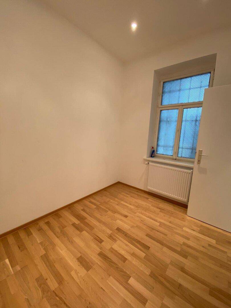 Gemütliches Schlafzimmer mit hellem Parkettboden und einem Fenster, ideal für Ruhe.