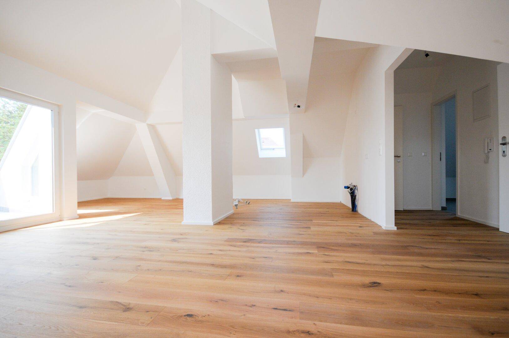 Heller Dachgeschossraum mit Holzboden und Zugang zu weiteren Zimmern, bereit für die Gestaltung.