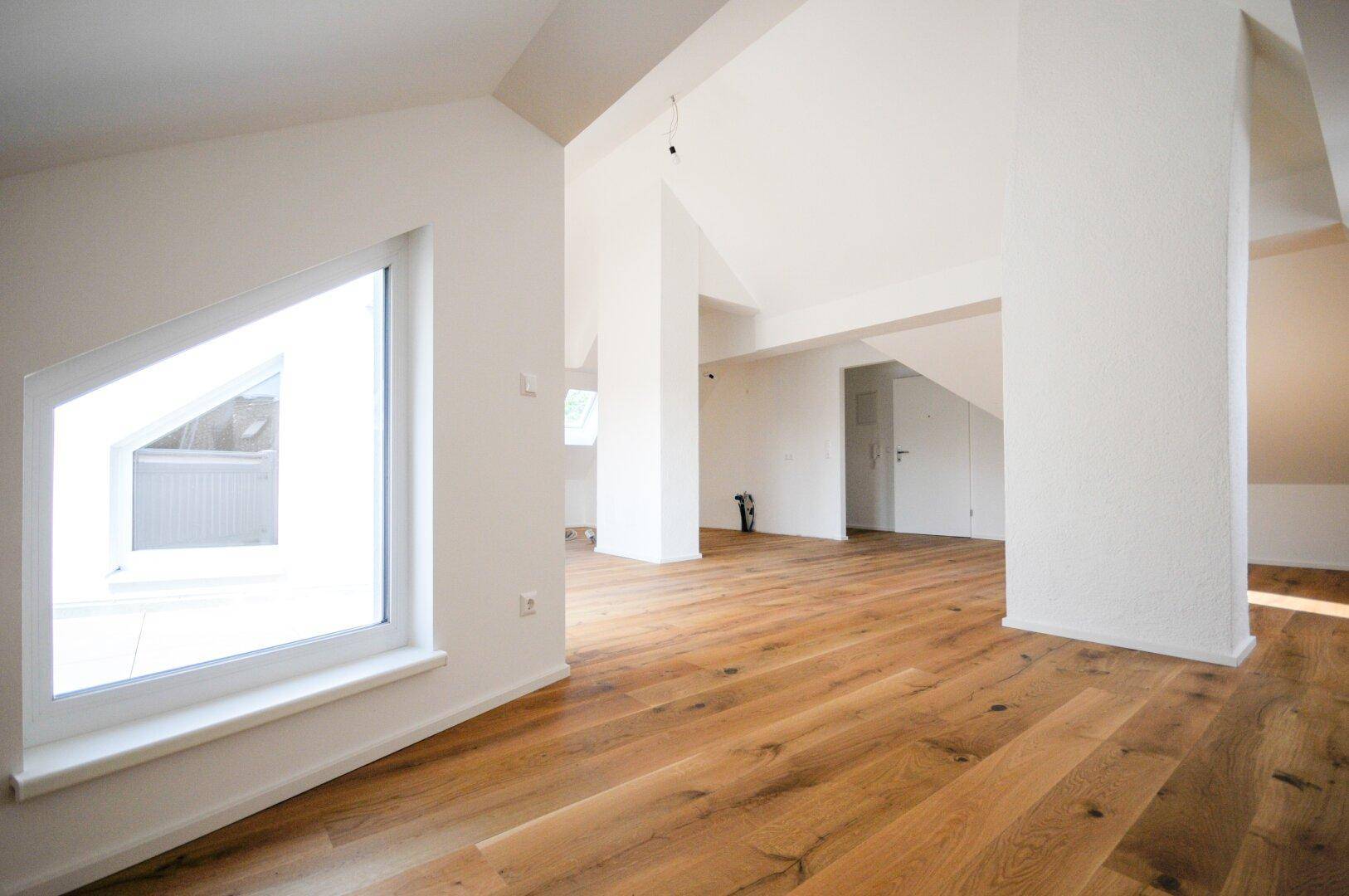 Geräumiger, heller Dachgeschossraum mit Holzboden und schrägen Wänden, ideal für individuelle Gestaltung.