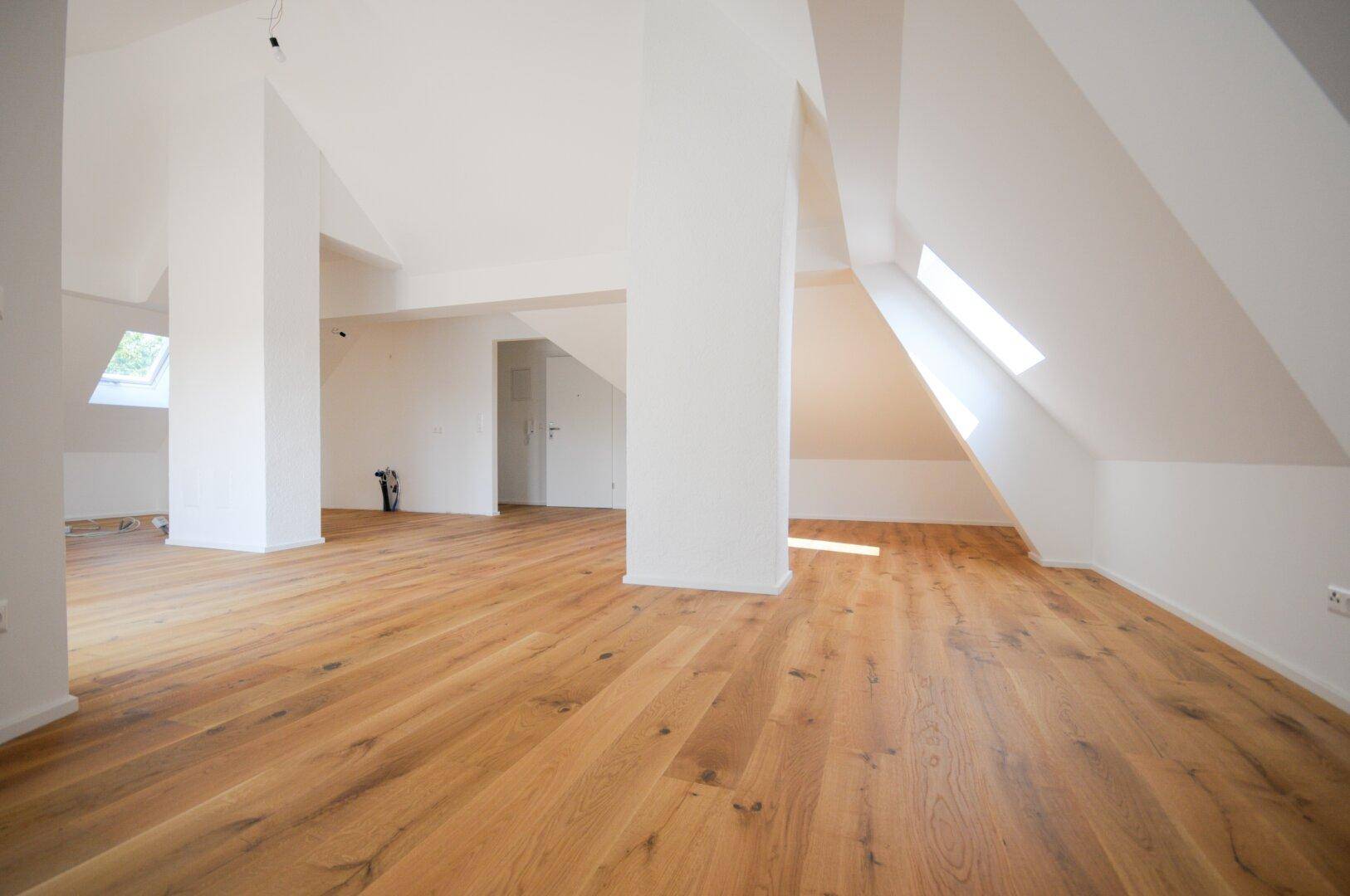 Weitläufiger Dachgeschossraum mit Holzboden, weißen Wänden und Dachfenstern, die viel Licht spenden.